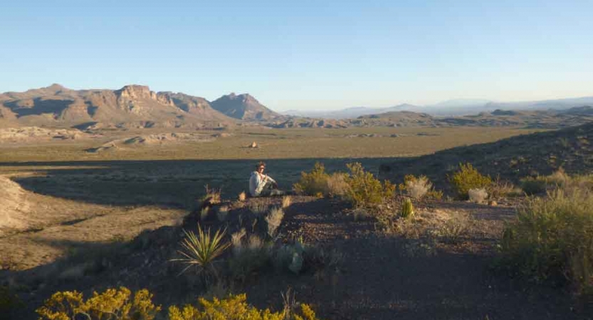 a gap year student sits on an elevated position, overlooking a desert landscape with a mountain in the background